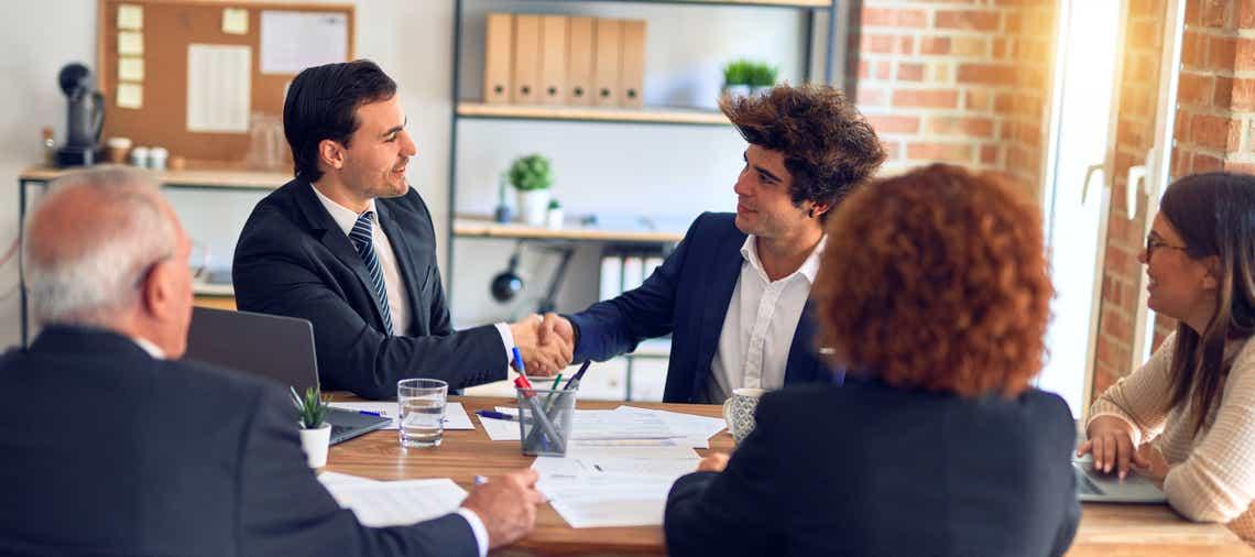 a customer success manager meeting with a group of clients - shaking hands because the group just improved their relationship.